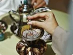 Hands holding a dallah over a tray of dates