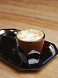 A latte in a dark cup on a black octagonal tray