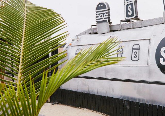 The silver Airstream behind a palm frond, burger and salt-shaker signs on the roof